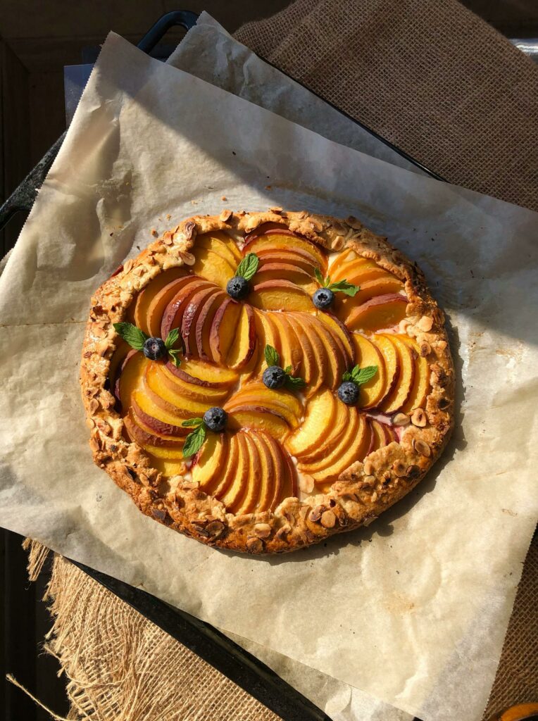 Delicious homemade peach galette with blueberries on parchment paper. Perfect summer dessert in natural light.